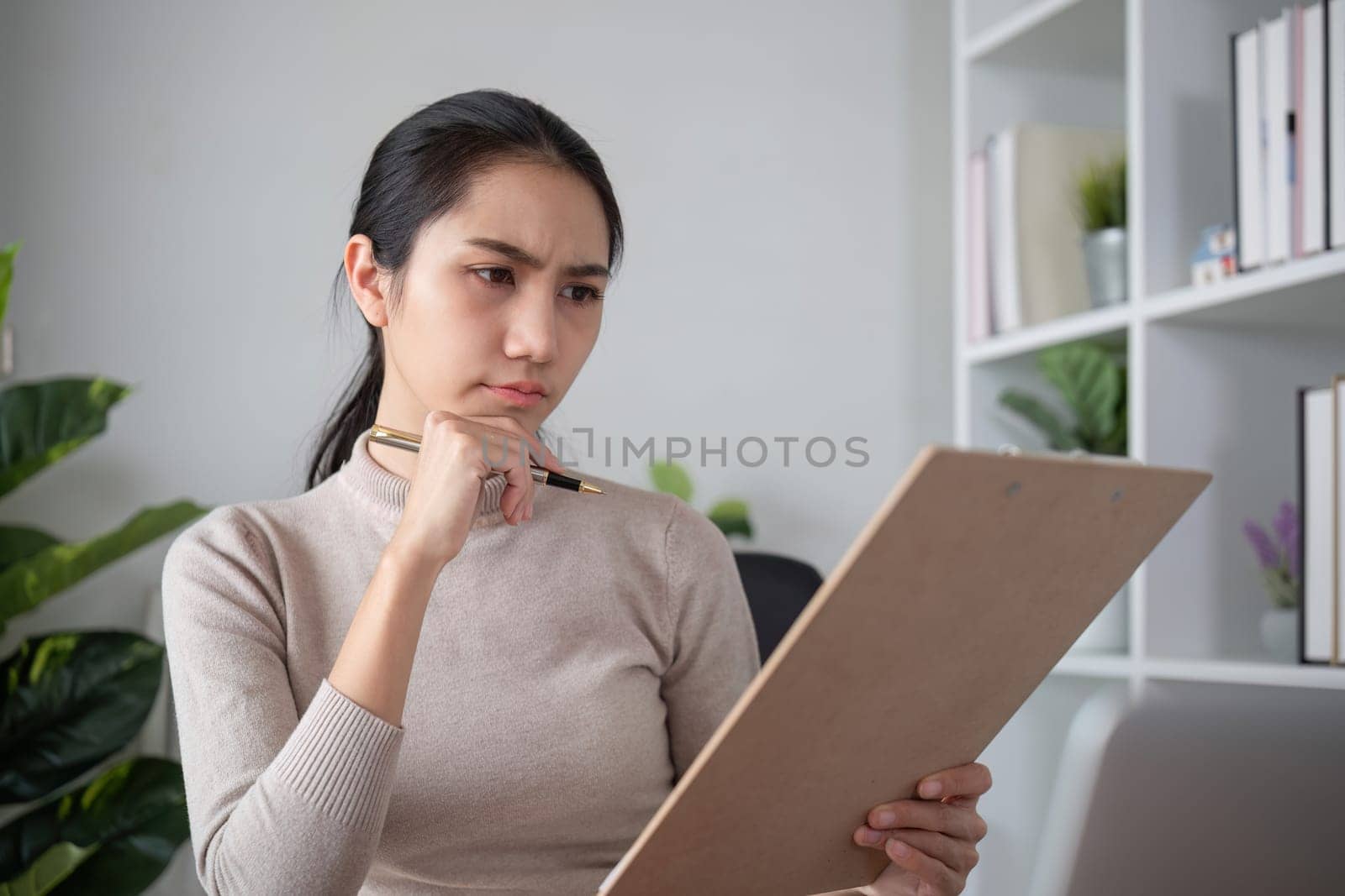 Asian businesswoman feeling tired and stressed over an unsuccessful business while working in a home office decorated with soothing green plants..