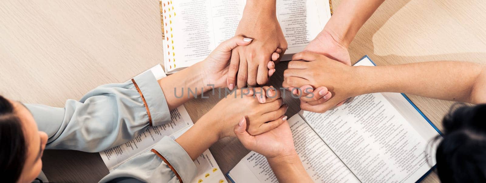 Cropped image of diversity people hand praying together at wooden church on bible book while hold hand together with believe. Concept of faith, god blessing concept. Top view. Burgeoning.