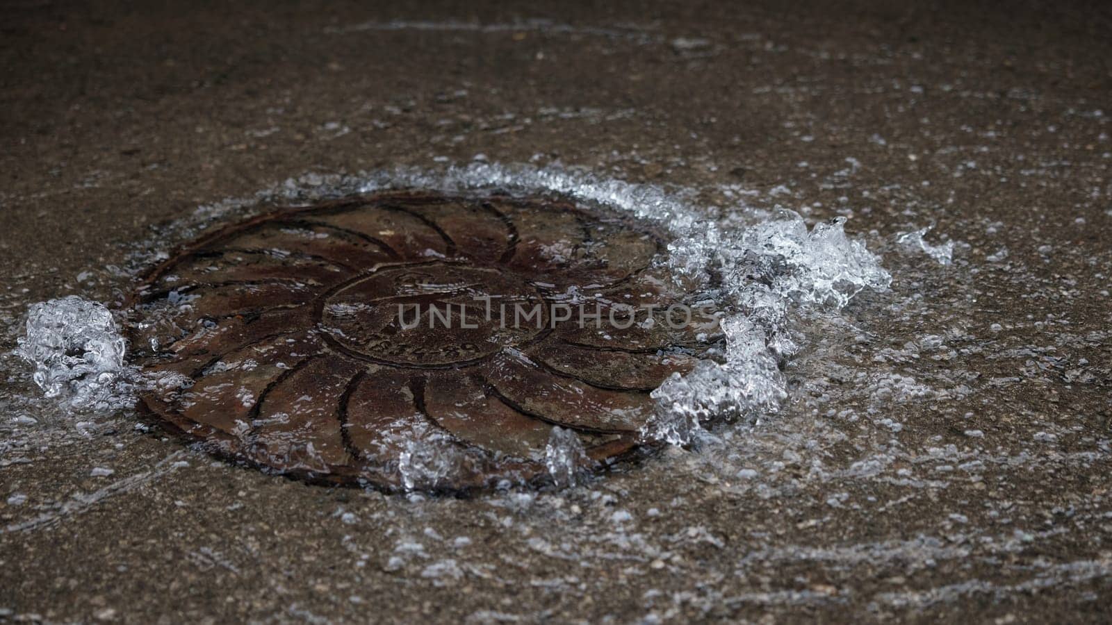 Water pipe burst, water Water flows out of the manhole onto the asphalt. The accident in the sewer. Leaking water supply system in the city on the road.
