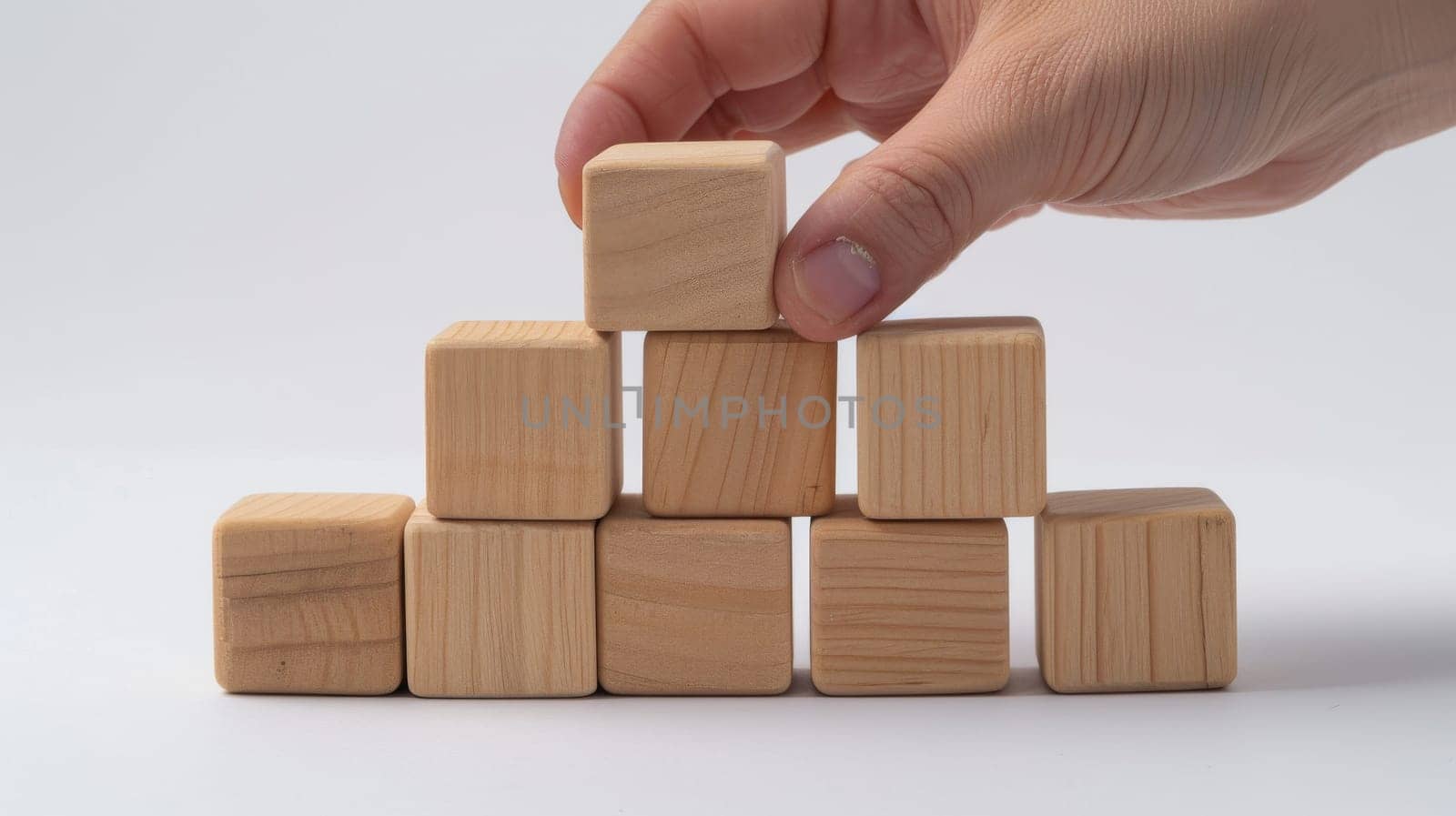 A man is holding a stack of wooden blocks. The blocks are of different sizes and are arranged in a pyramid shape. Concept of creativity and playfulness, as the man is holding the blocks in his hands