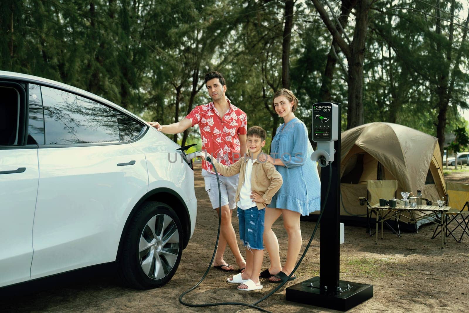 Outdoor adventure and family vacation camping in nature travel by eco friendly car for sustainable future. Lovely family recharge EV car with EV charging station in campsite. Perpetual