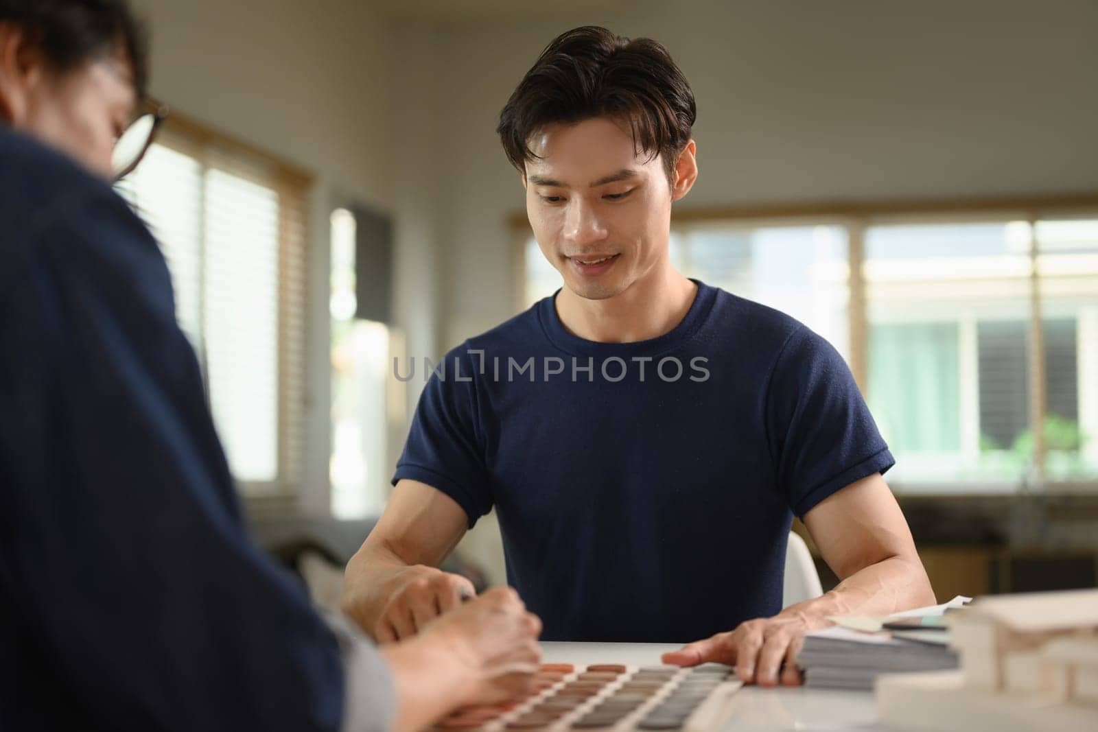 Smiling Asian male client choosing paint colors for renovation at office