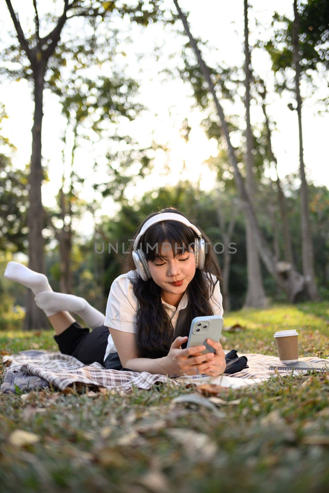 Portrait of relaxed young woman listening to music and using mobile phone on grass by prathanchorruangsak