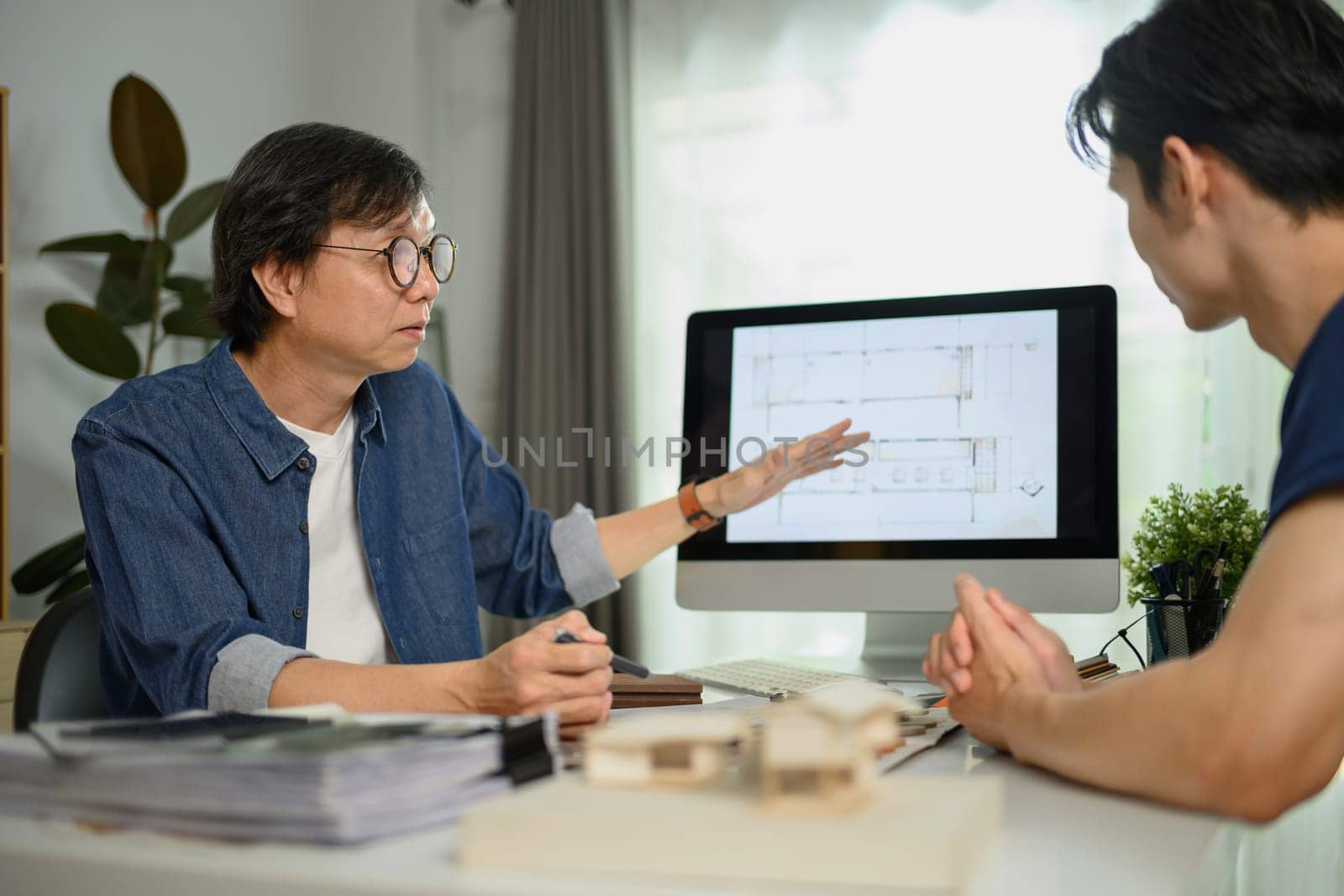 Professional interior designer sharing ideas and showing architectural plan to male client by prathanchorruangsak
