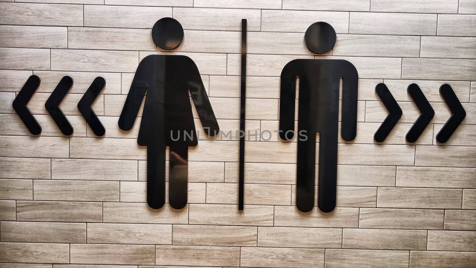 Male and Female Restroom Symbols on Wooden Wall With Directional Arrows. Gender-specific bathroom signs on wood surface
