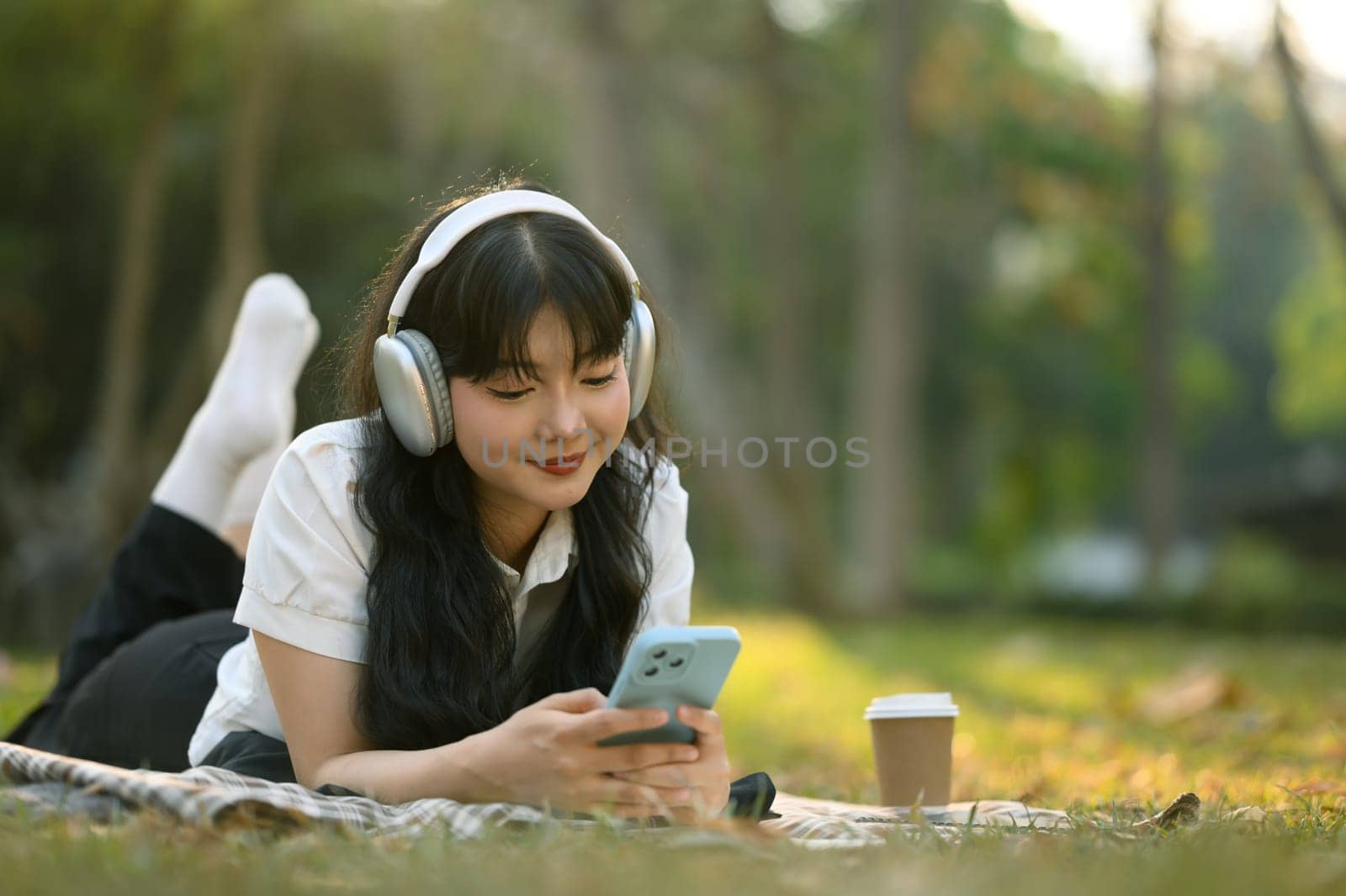 Pretty young woman listening music with headphones and using mobile phone in the summer park.
