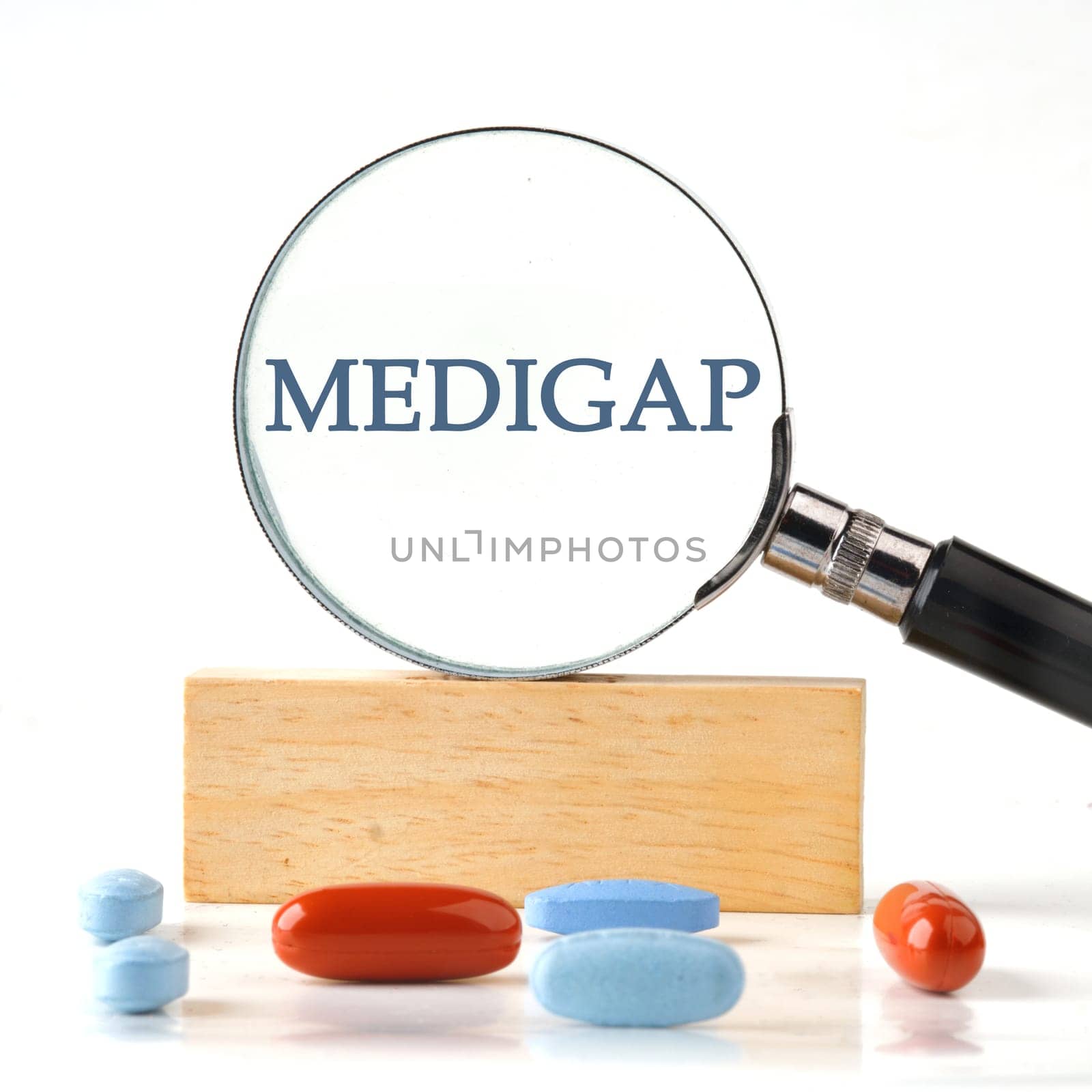 Medical concept. MEDIGAP through a magnifying glass on a wooden block with vitamins, pills in the foreground