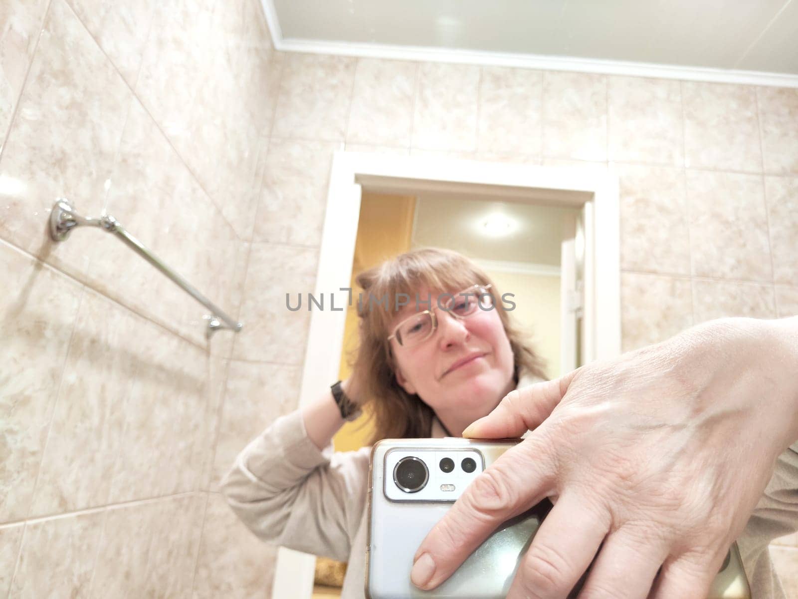 Mature woman captures her reflection while taking selfie. The reflection of middle aged girl with a phone in the mirror. Partial focus