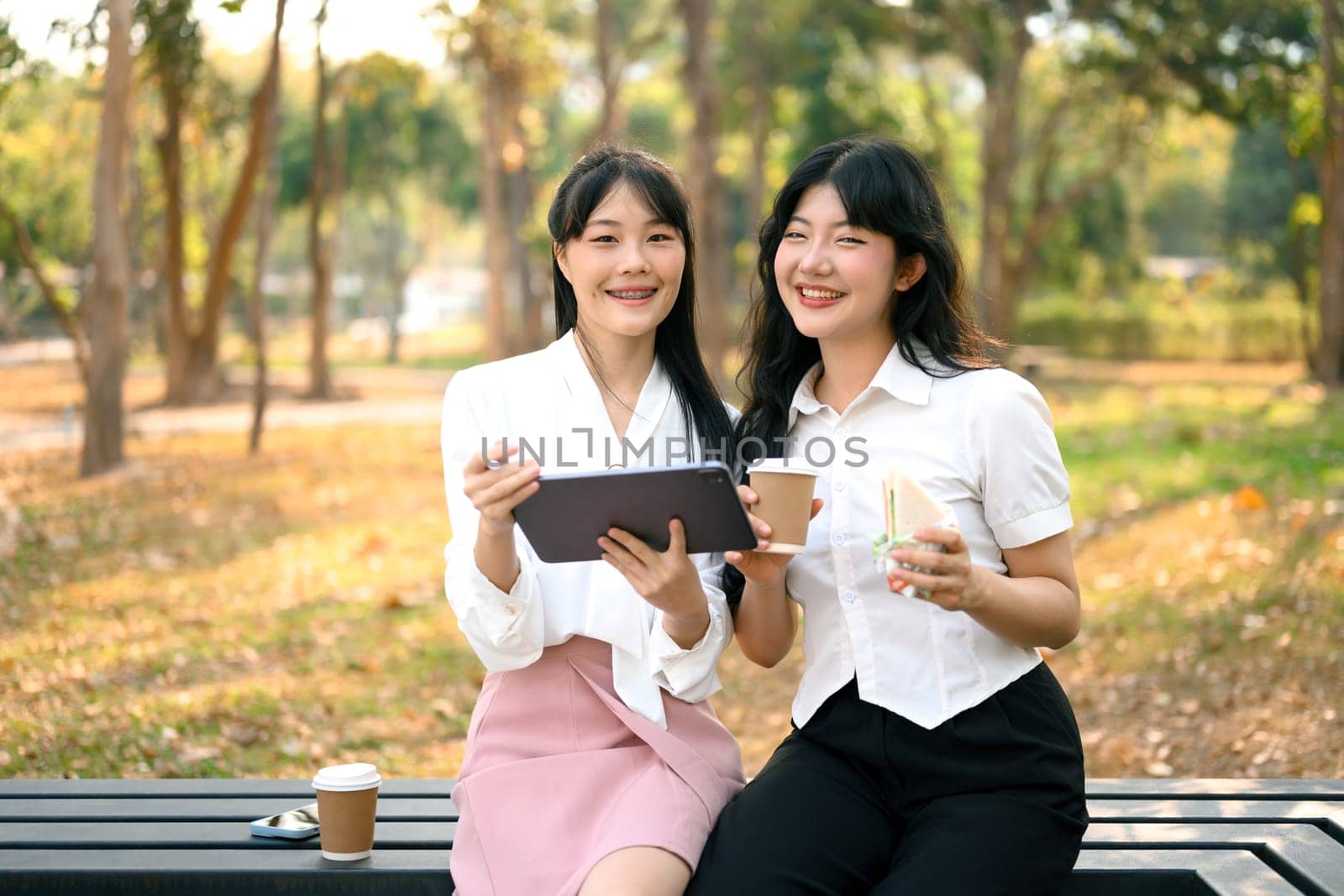 Two cheerful office workers using digital tablet and chatting on a coffee break at outdoor.