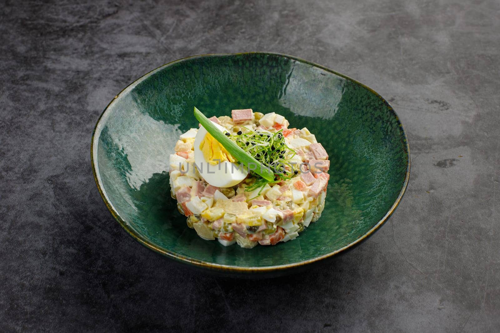 Traditional Russian snack. Salad olivie on a plate on a gray stone background. Restaurant menu