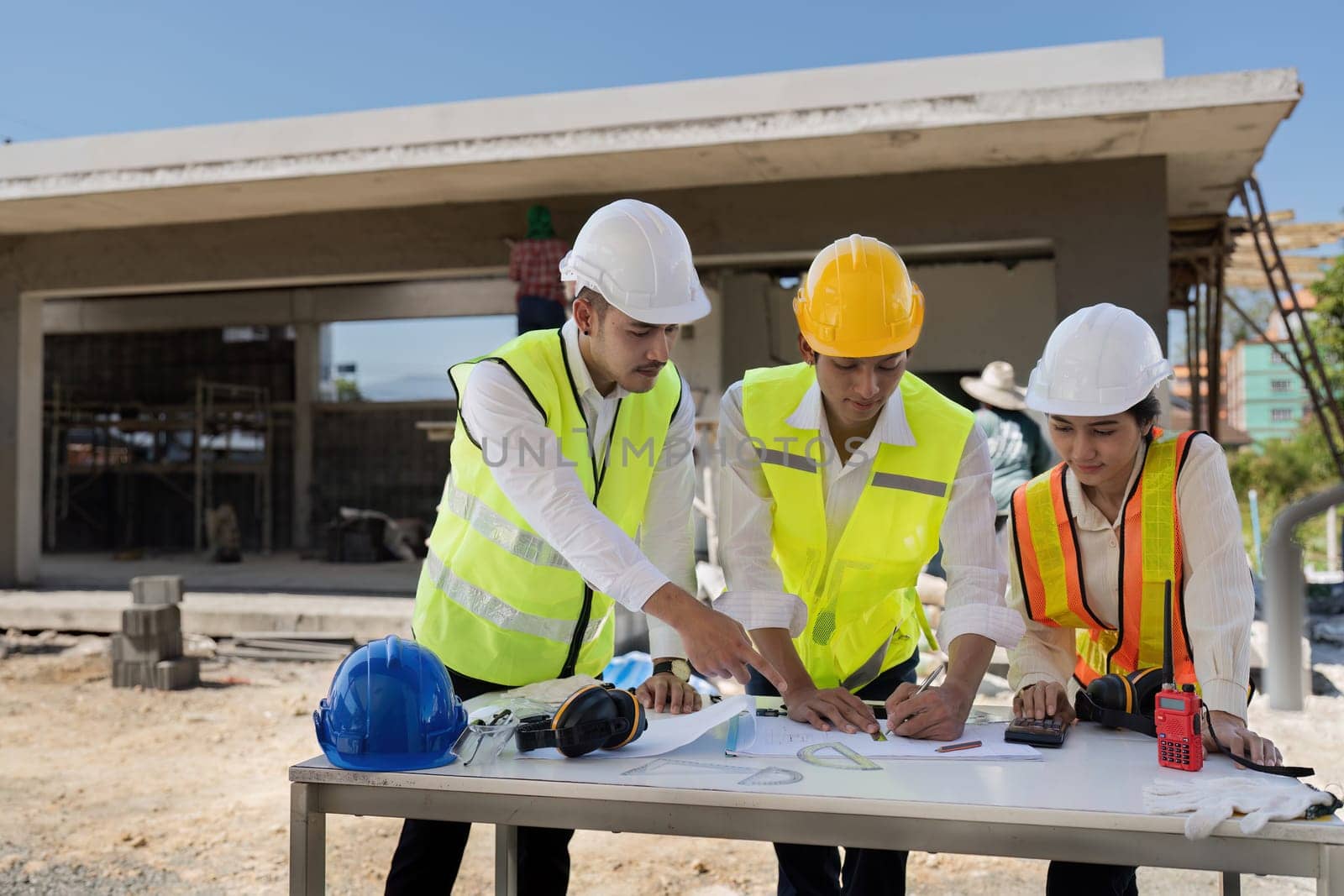 Two people are working on a blueprint, one of them is wearing a safety vest. Concept of collaboration and focus as the two individuals work together to create a detailed plan