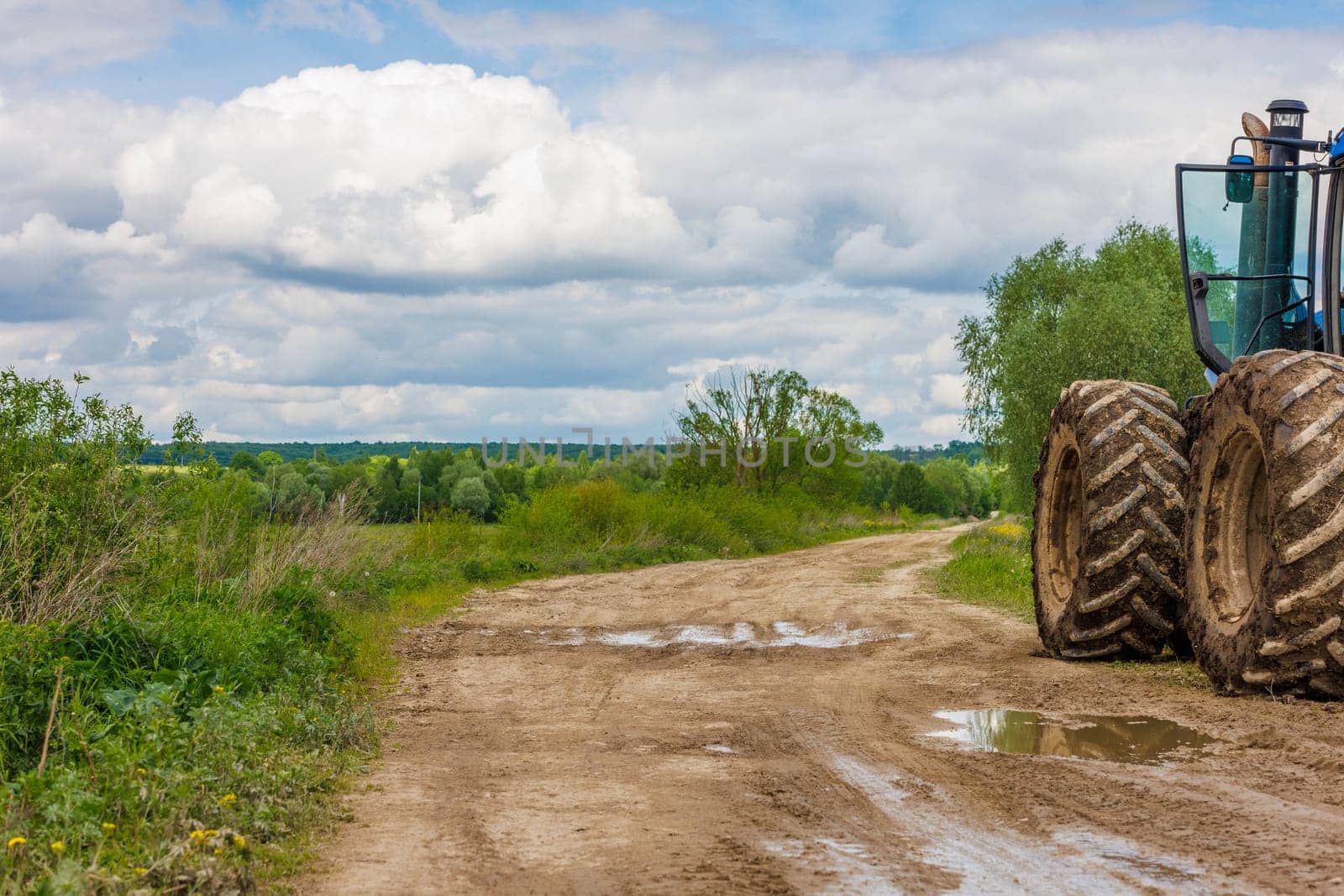 Tractor with large wheels on the edge of a dirt road at summer day with cloudy sky. by z1b
