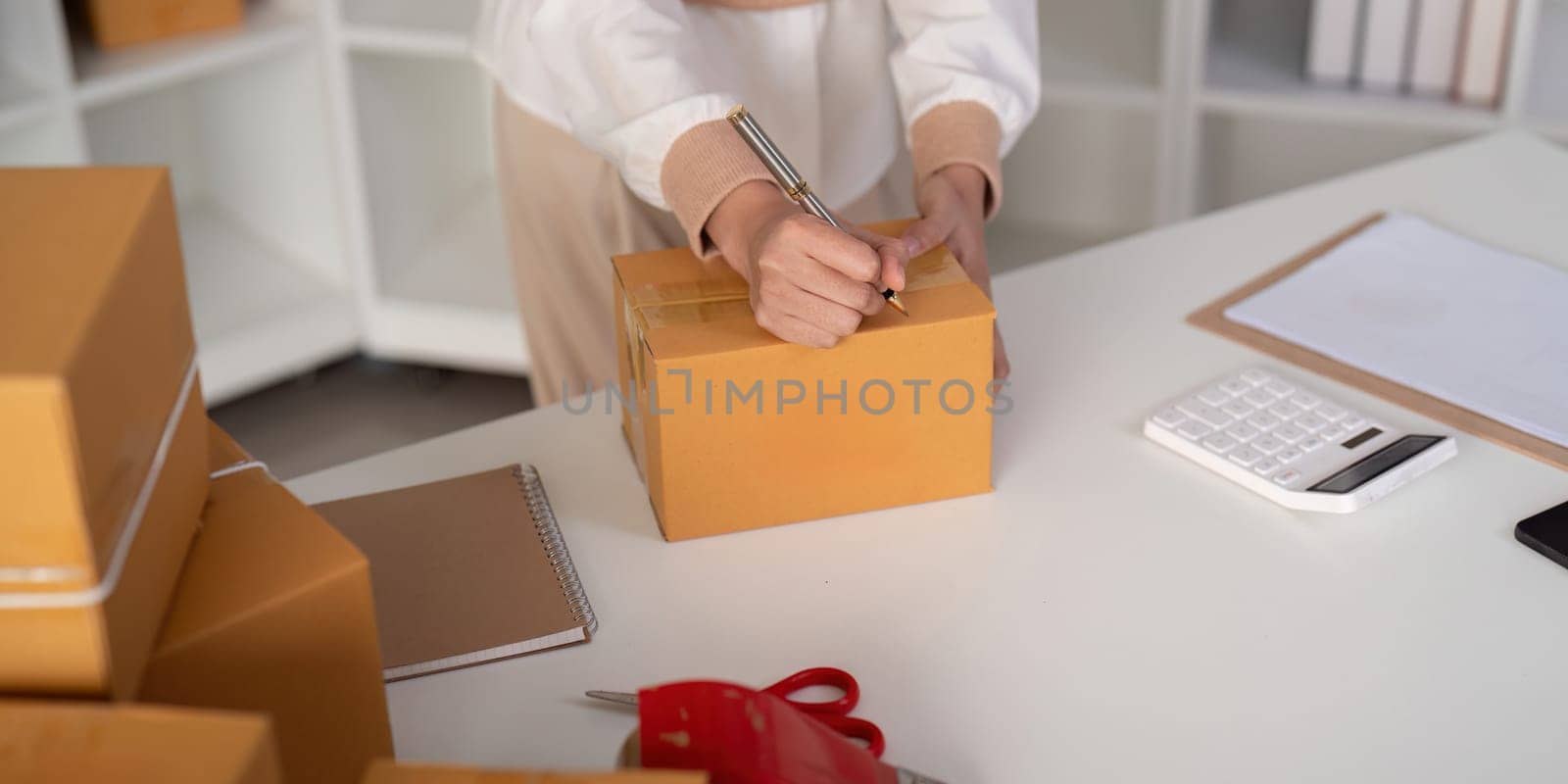 Woman is writing a list of customer on paper before shipping to them, she runs an ecommerce business on websites and social media. Concept of selling products online by nateemee