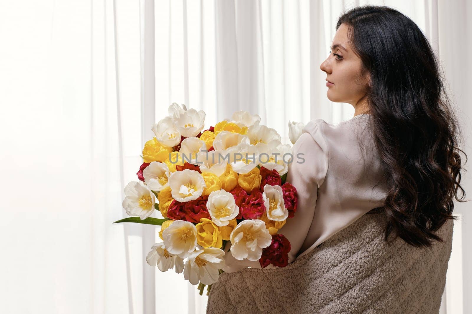 Beautiful curly woman with spring flowers tulips in hands. Women's Day. copy space