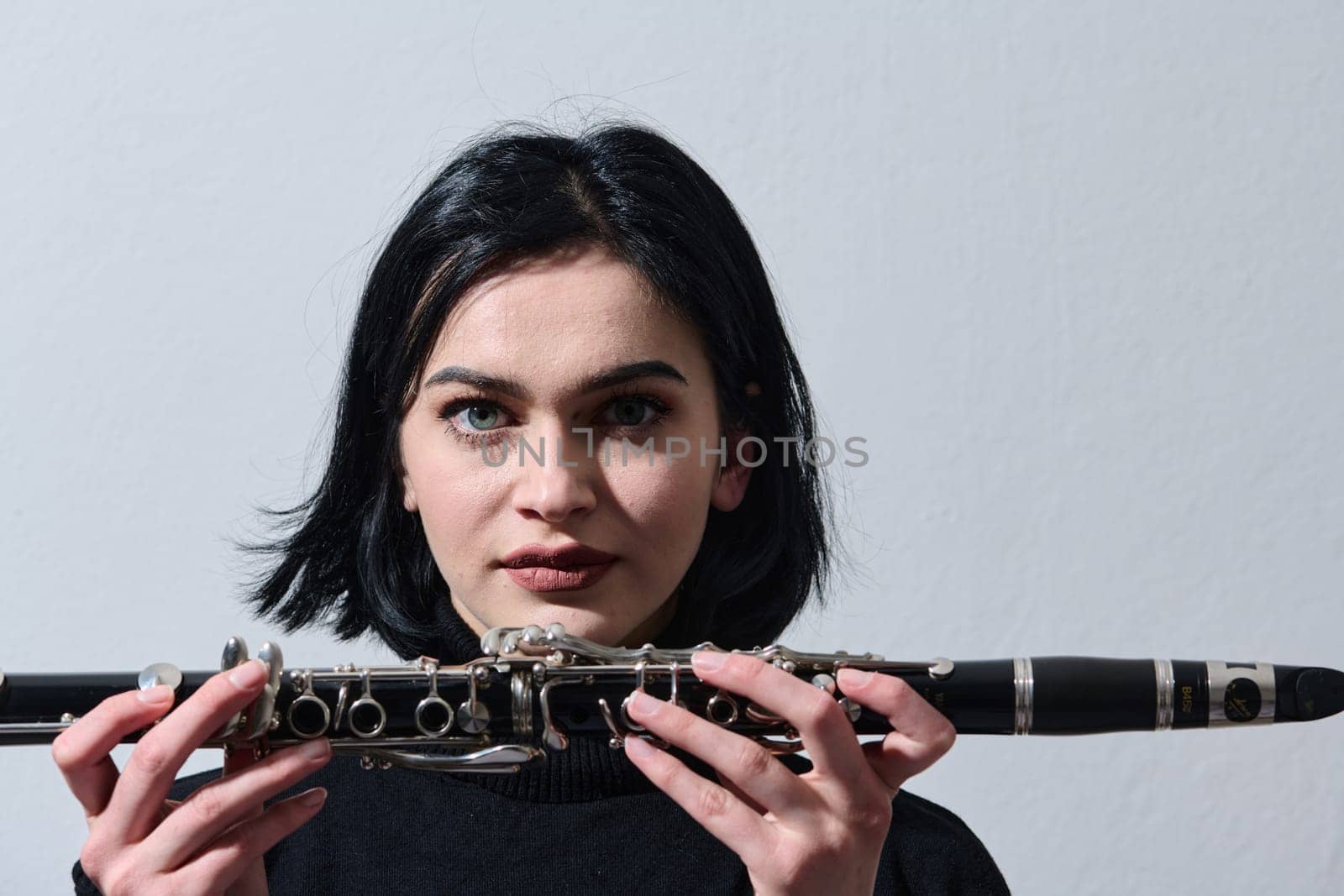 A talented brunette musician showcases her artistry as she gracefully holds and plays the clarinet against a pristine white background