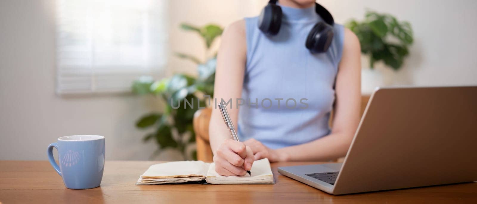 Happy young woman asian in headphones looking at laptop making note, girl student talking by video conference call, online training.