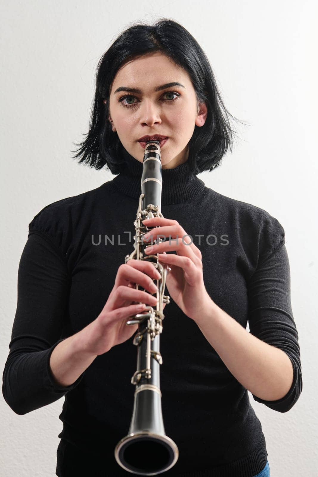 A talented brunette musician showcases her artistry as she gracefully holds and plays the clarinet against a pristine white background