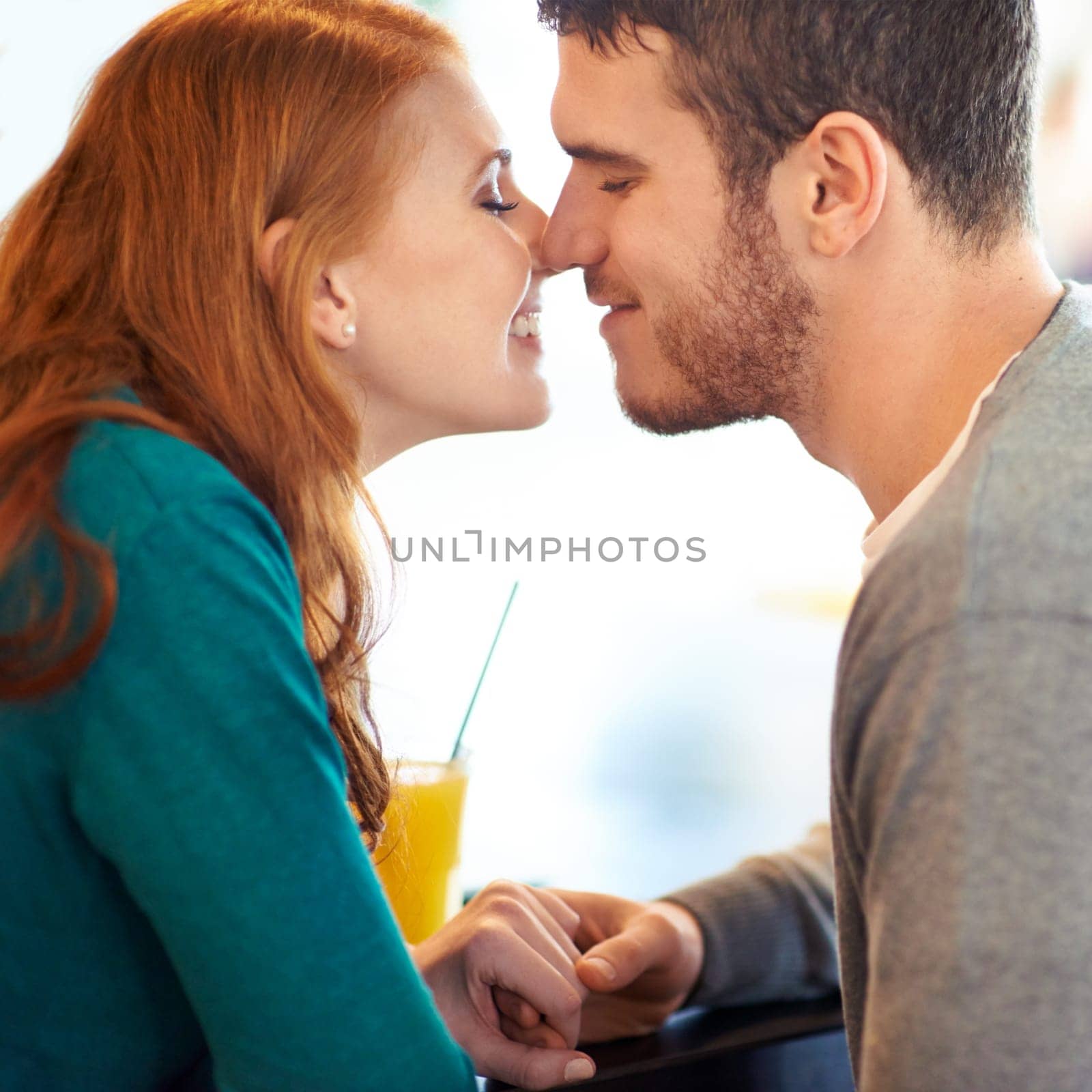 Couple, date and kiss with love, coffee shop or restaurant with happiness together. Man, woman and romance for relationship, care and smile for flirting on break for relax or bonding in cafe by YuriArcurs