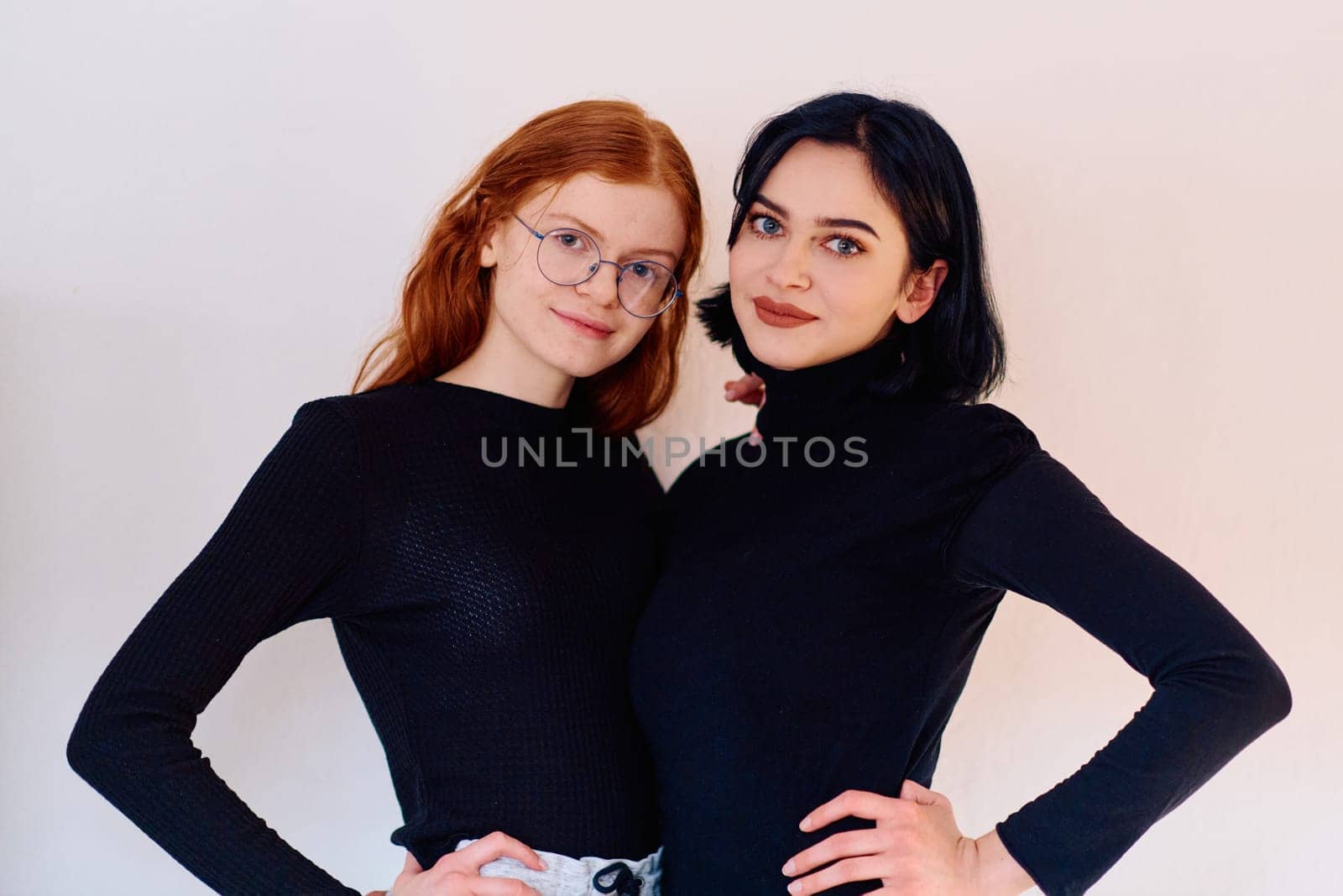 Two sisters, one brunette and one redhead, share a tender embrace, epitomizing the enduring bond of sisterhood against a backdrop of pristine white.