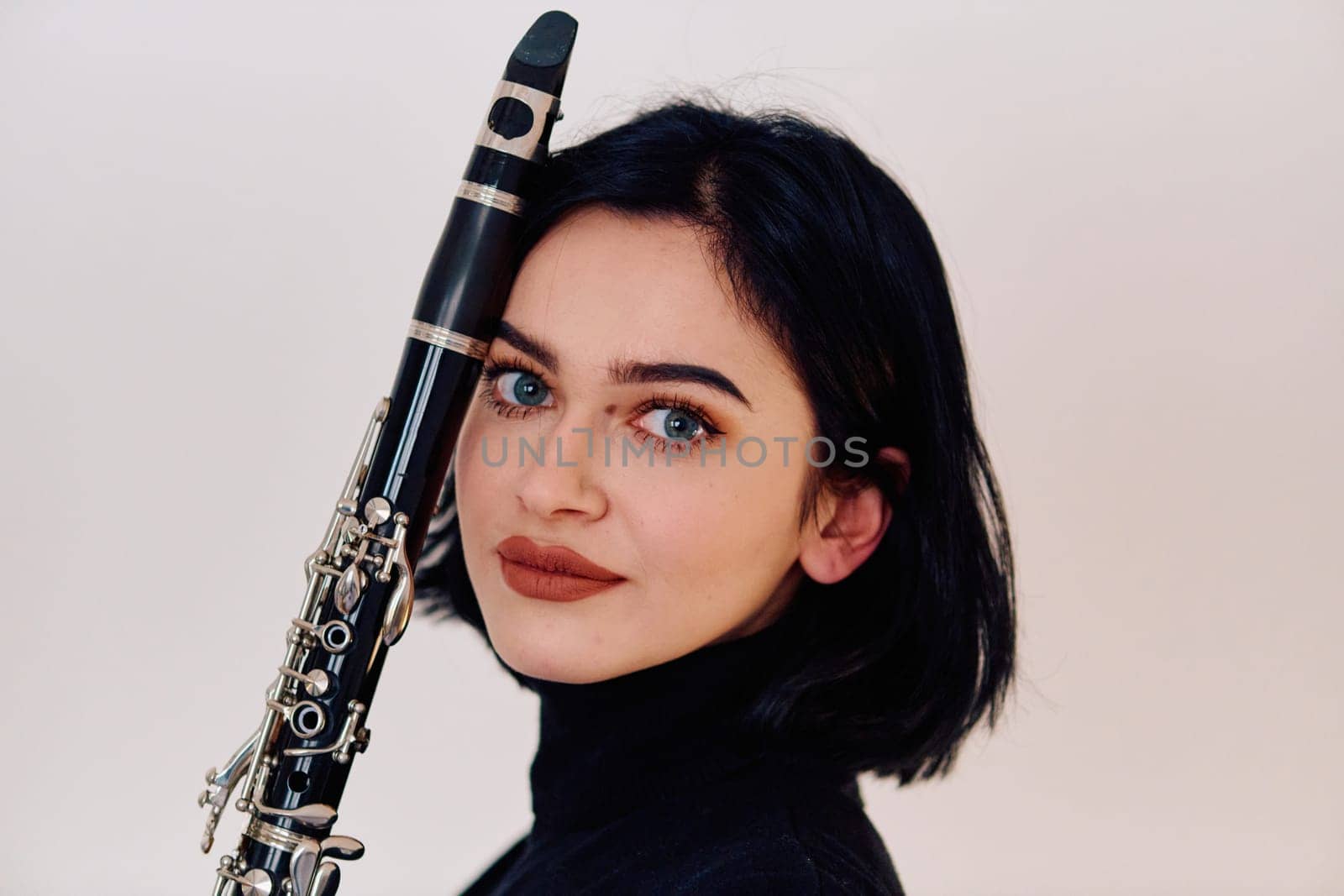 A talented brunette musician showcases her artistry as she gracefully holds and plays the clarinet against a pristine white background