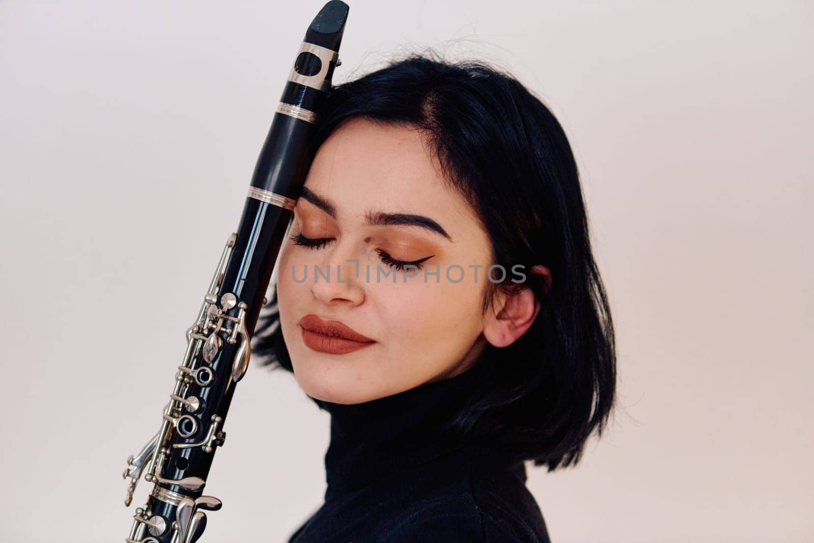 A talented brunette musician showcases her artistry as she gracefully holds and plays the clarinet against a pristine white background