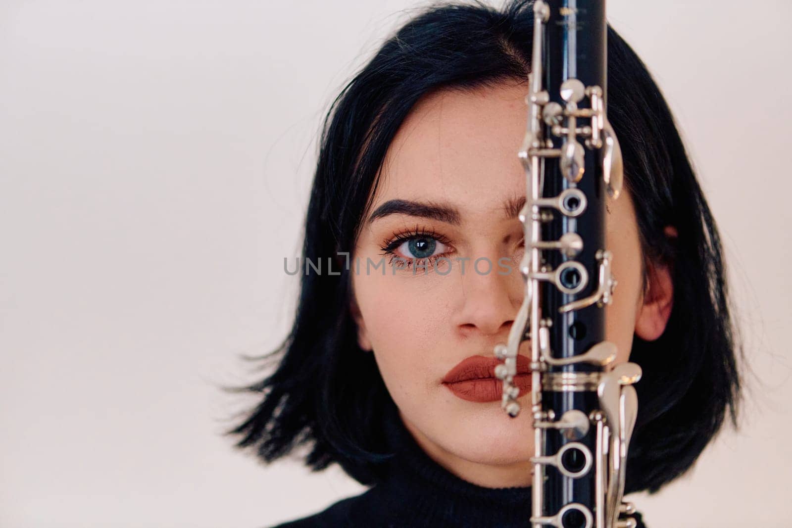 A talented brunette musician showcases her artistry as she gracefully holds and plays the clarinet against a pristine white background