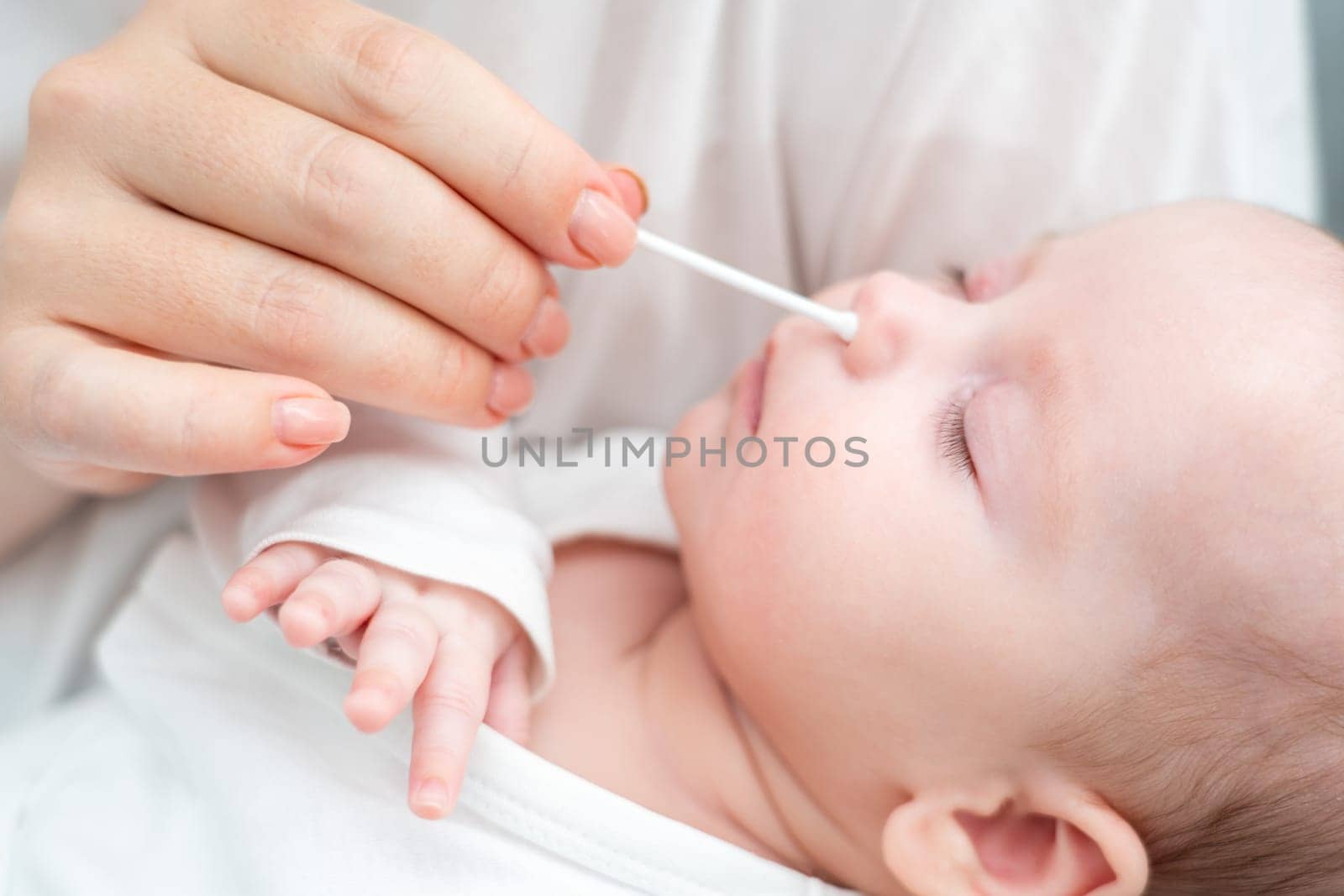 Mother applies age-old practices, cleaning her newborn's nose with soft precision and genuine