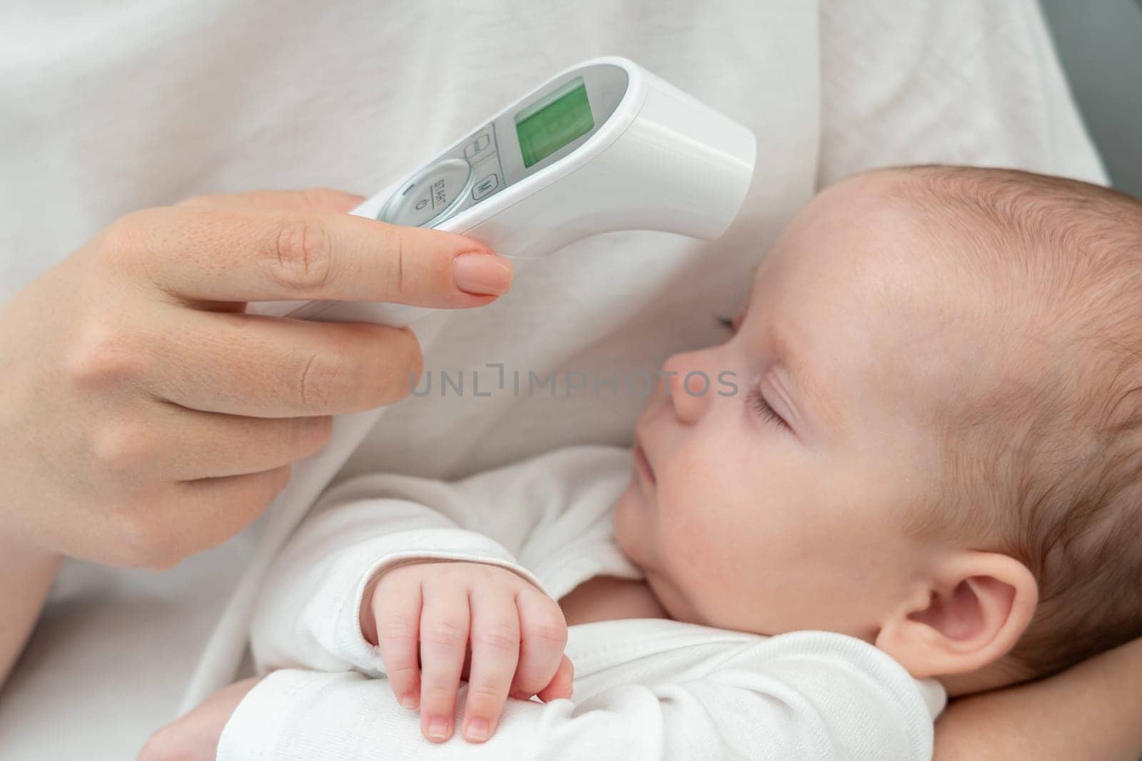 A caring mother uses an electronic thermometer, pointing it to her newborn's forehead to measure