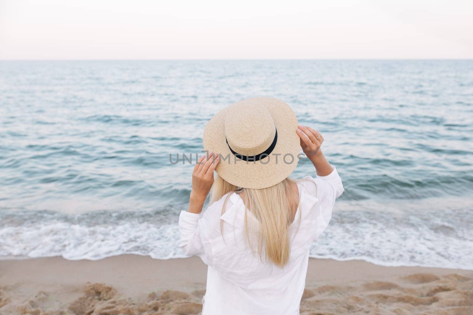 Pretty slim tanned blonde stylish woman in a straw hat posing on a paradise tropical beach.
