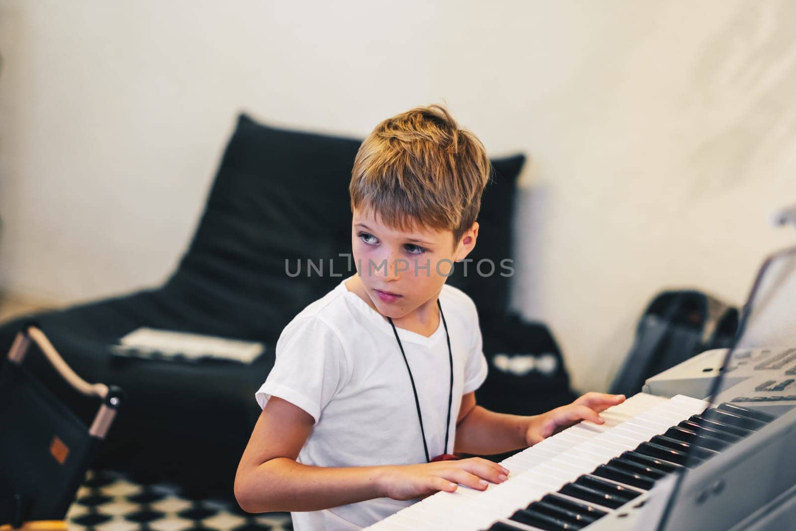 Young boy Portrait sitting at digital piano Playing keyboard focused kid activity indoors press on Key learning to play music room Hobby.