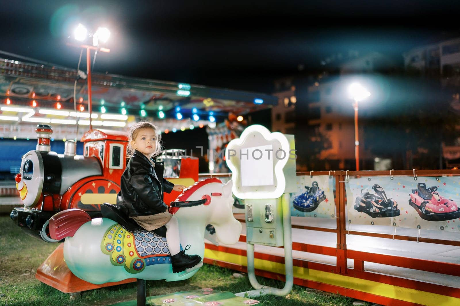 Little girl sits on an electric rocking horse swing at a fair and looks away. High quality photo