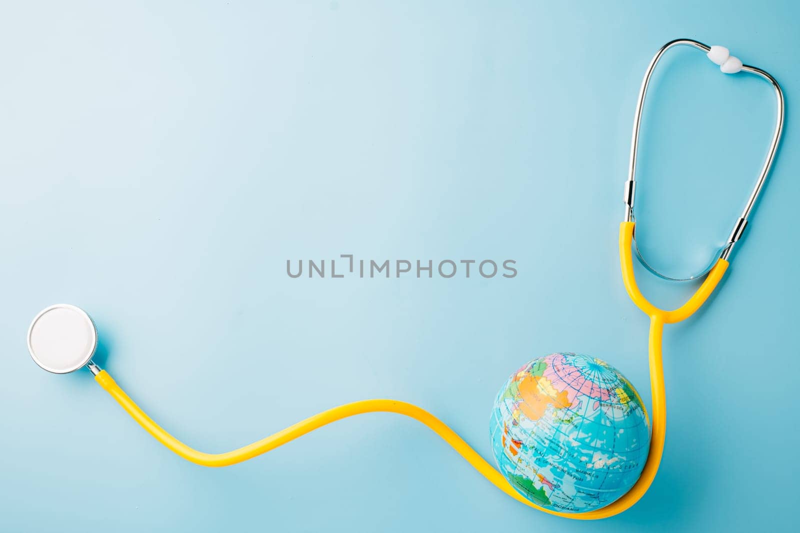 World Health Day. Yellow doctor stethoscope and world globe isolated on pastel blue background with copy space for text, Save world day, Green Earth Environment, Healthcare and medical concept