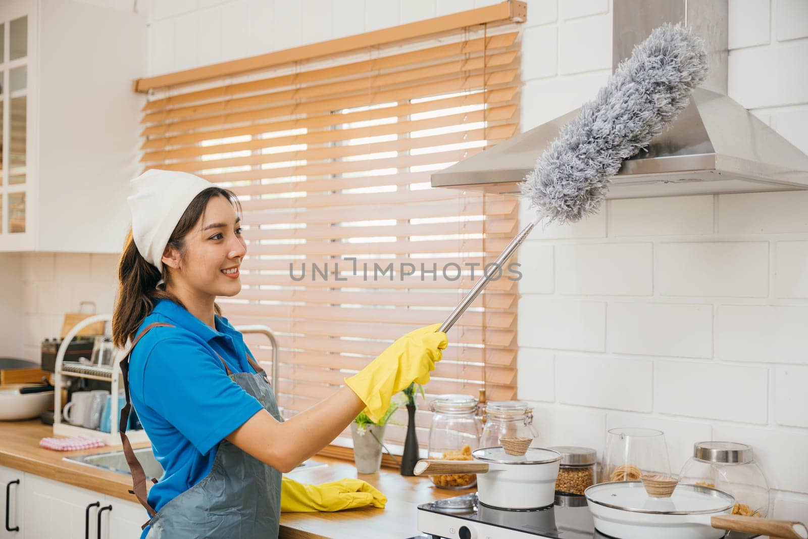 Maid in workwear and gloves cleans home dusts kitchen ventilation. Emphasizing modern housework hygiene equipment in use. Clean air brush maid service portrait. maid housekeeping concept.