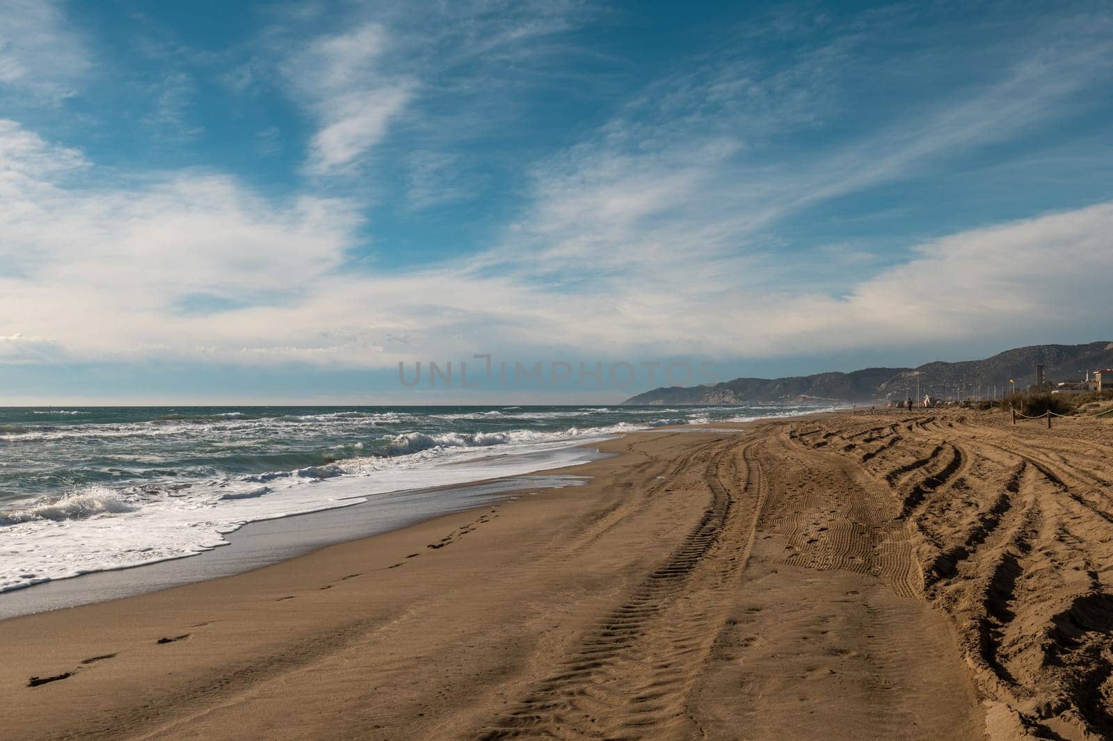Deserted Sandy Beach with Foamy Waves and Tire Tracks under a Vast Blue Sky by apavlin