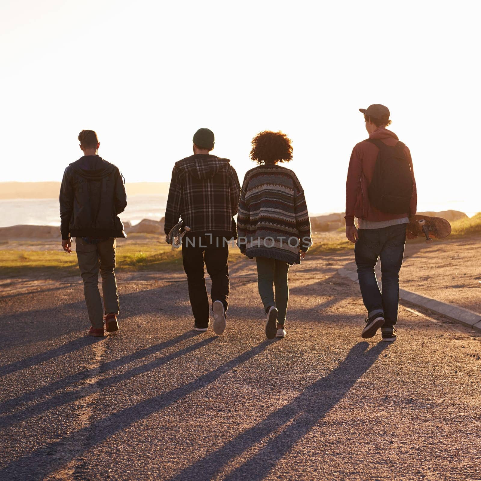 Walking, sunset and back of friends on vacation, travel or holiday together with skateboard. Summer, evening and group of young people by outdoor ocean or sea on weekend trip for bonding in nature