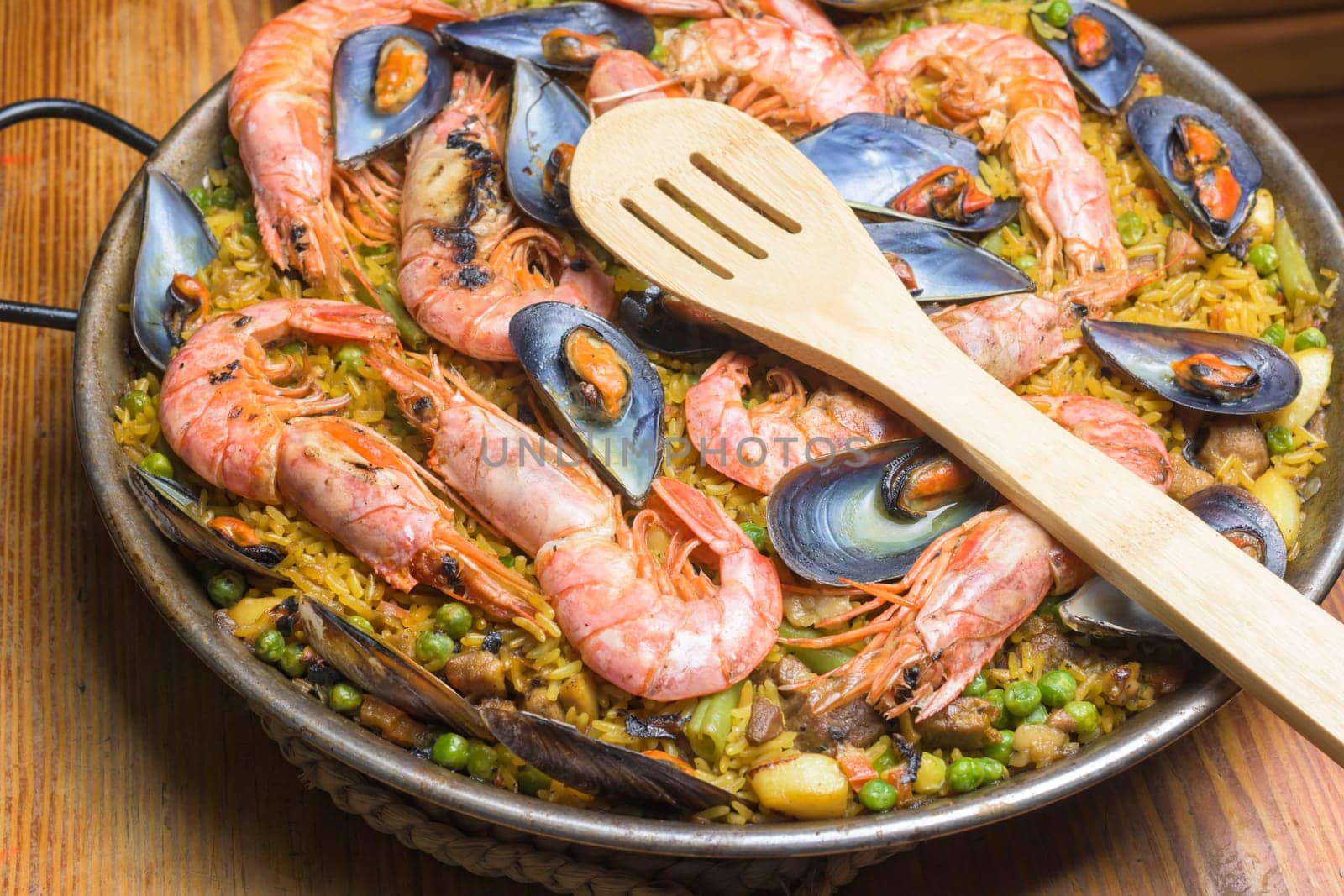 A paella full of seafood, peas, and rice served in a pan with a wooden spoon, typical Spanish cuisine, Majorca, Balearic Islands, Spain by carlosviv