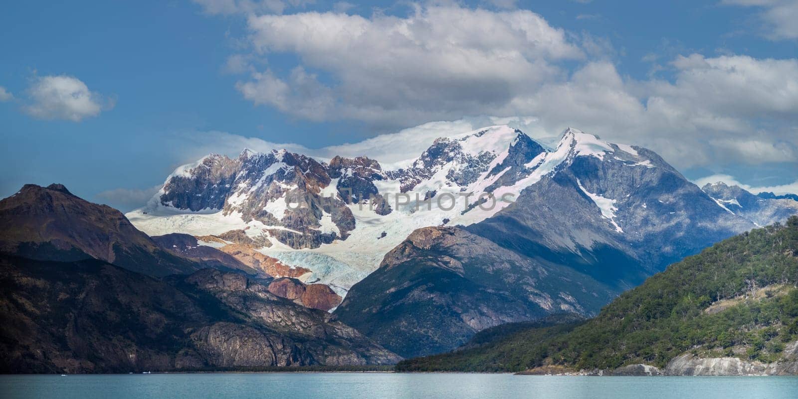 Captivating glacier nestled between craggy peaks beside a tranquil, mirror-like lake.
