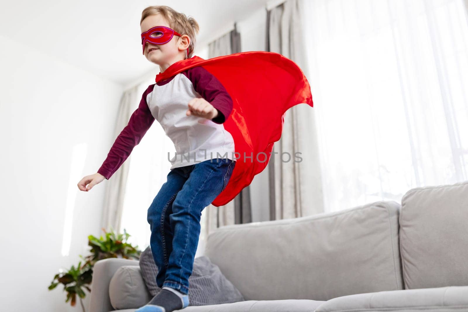Child in superhero costume playfully 'flies' inside home