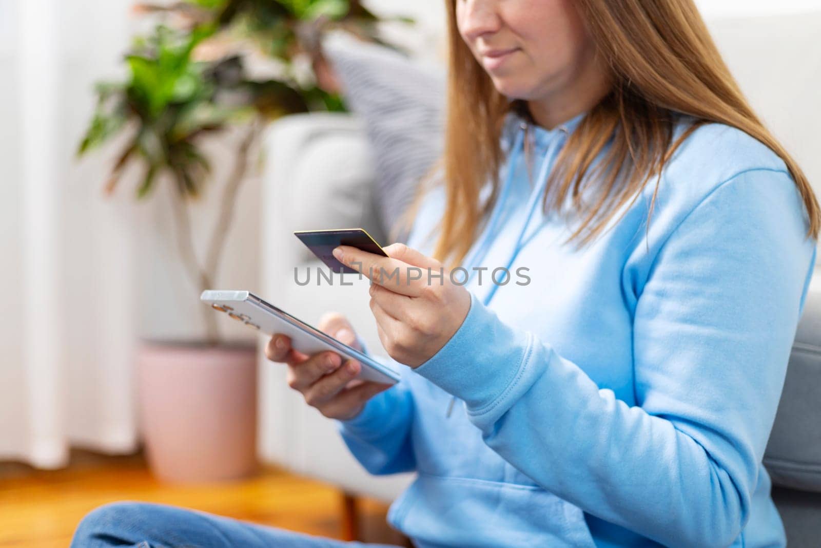 Focused woman using smartphone and credit card for online shopping, sitting on a couch at home.