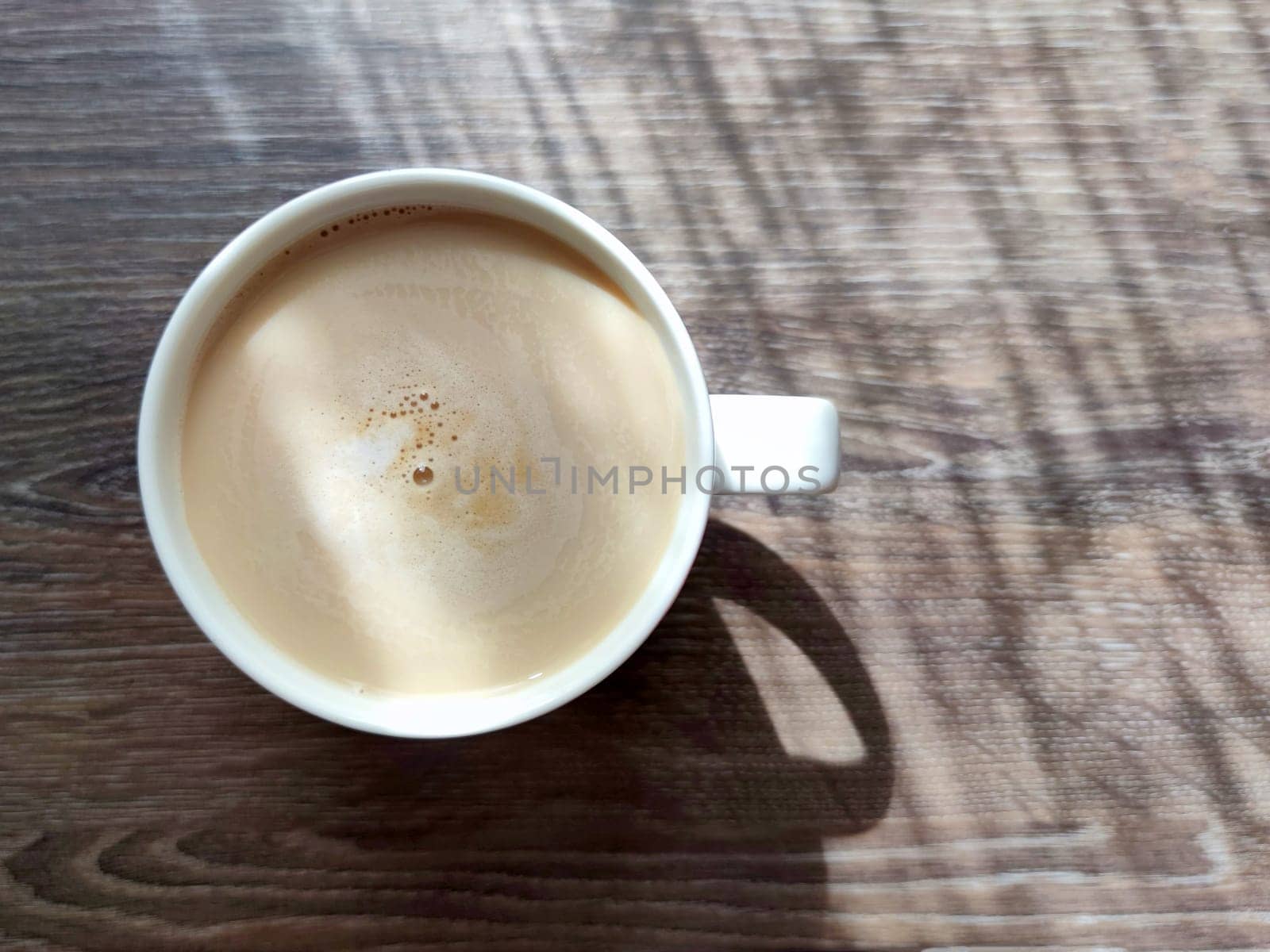 coffee with milk, cappuccino in a cup on a wooden table in sunlight, top view by Annado