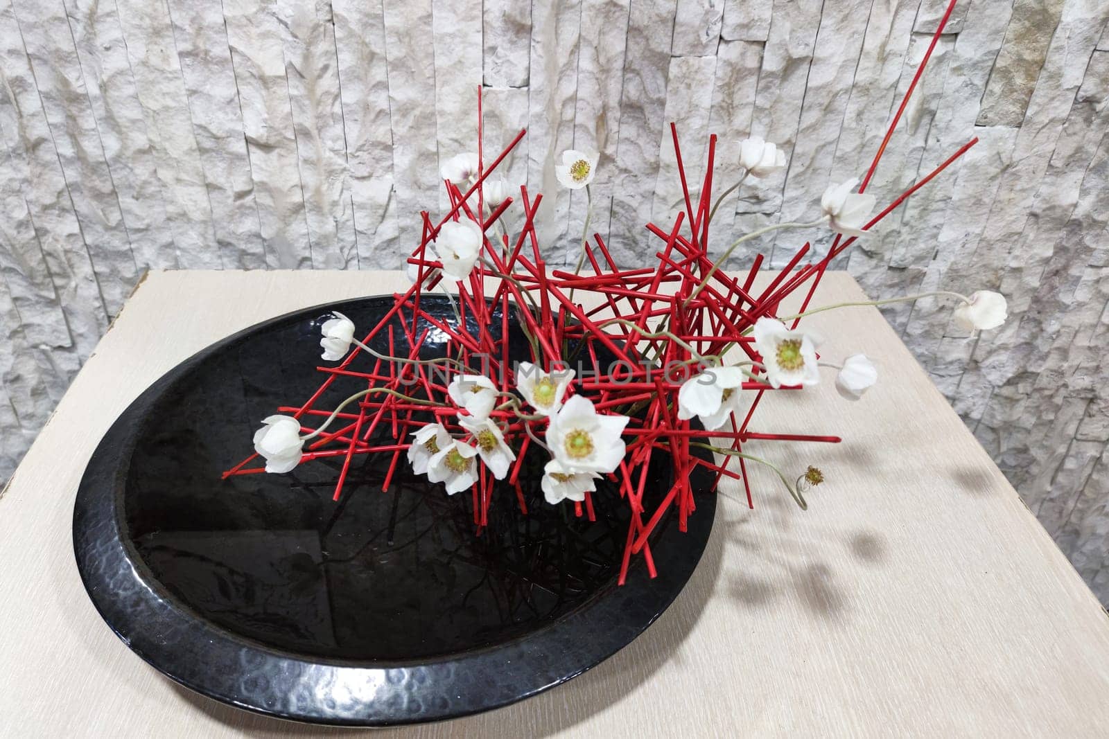 ikebana of red twigs and white flowers in a flat vase with water by Annado