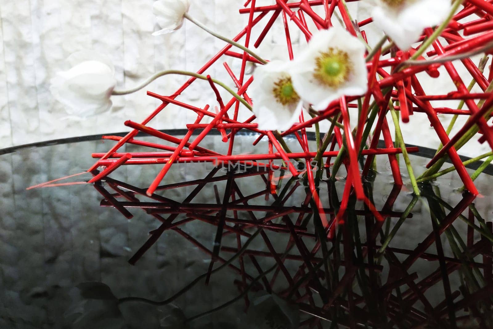 ikebana of red twigs and white flowers in a flat vase with water close-up
