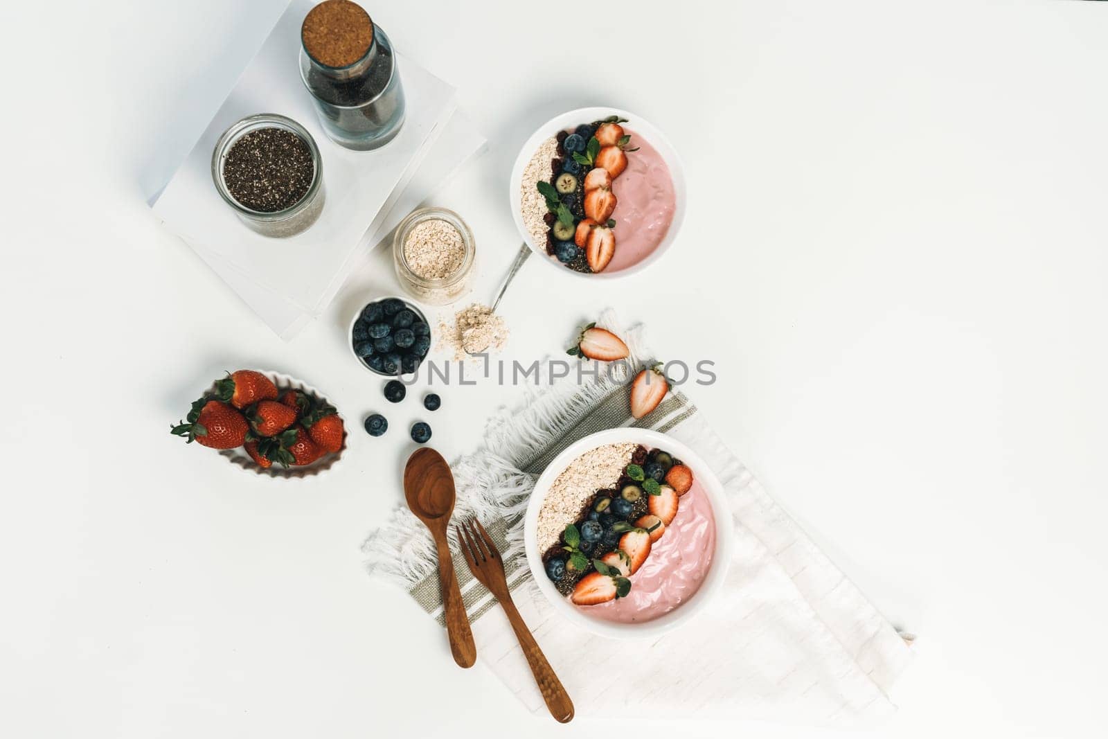 Presented by fruits putting yogurt toppings with strawberry, berry, oats, raisins and chia seed decorated by peppermint in white blow. Pink background. Set of healthy dairy product choice. Pecuniary.