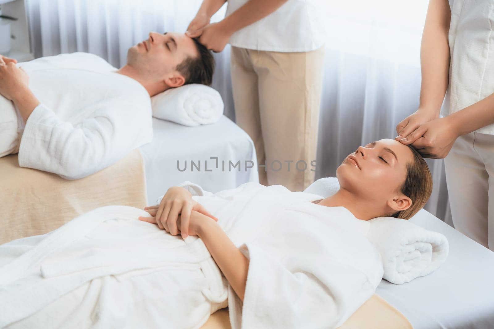 Caucasian couple enjoying relaxing anti-stress head massage and pampering facial beauty skin recreation leisure in dayspa modern light ambient at luxury resort or hotel spa salon. Quiescent