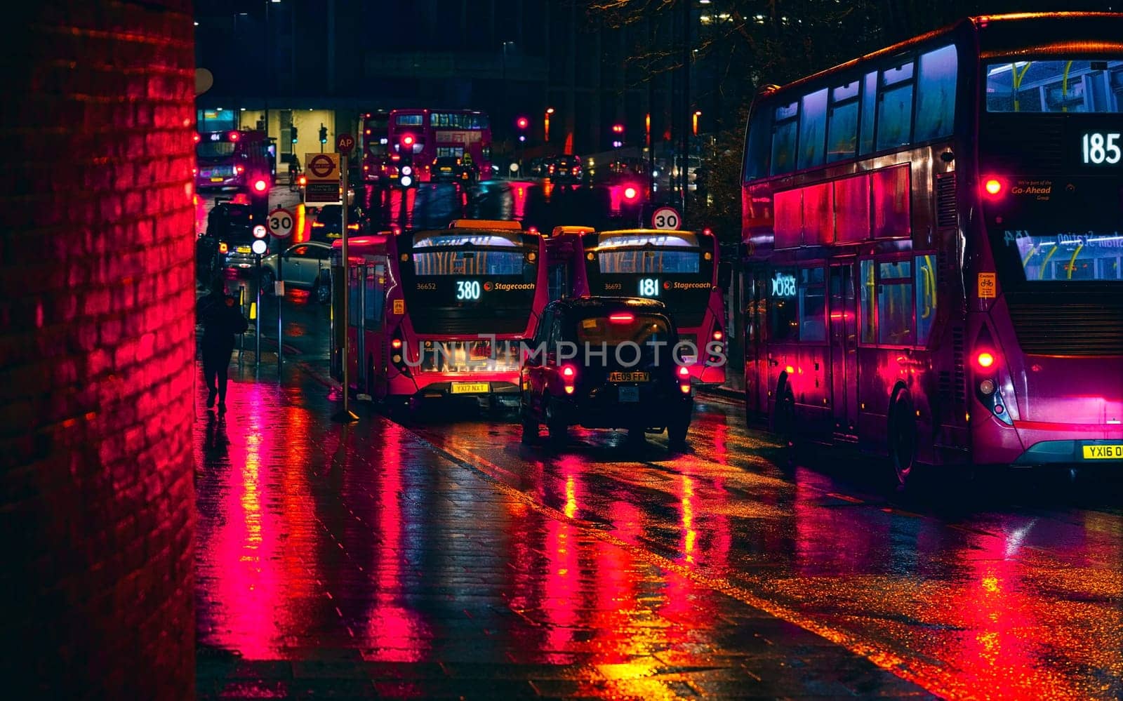 London, United Kingdom - February 01, 2019: Buses and taxis stuck in heavy traffic on a rainy evening near Lewisham station, bright red lights reflected in wet road and pavement by Ivanko