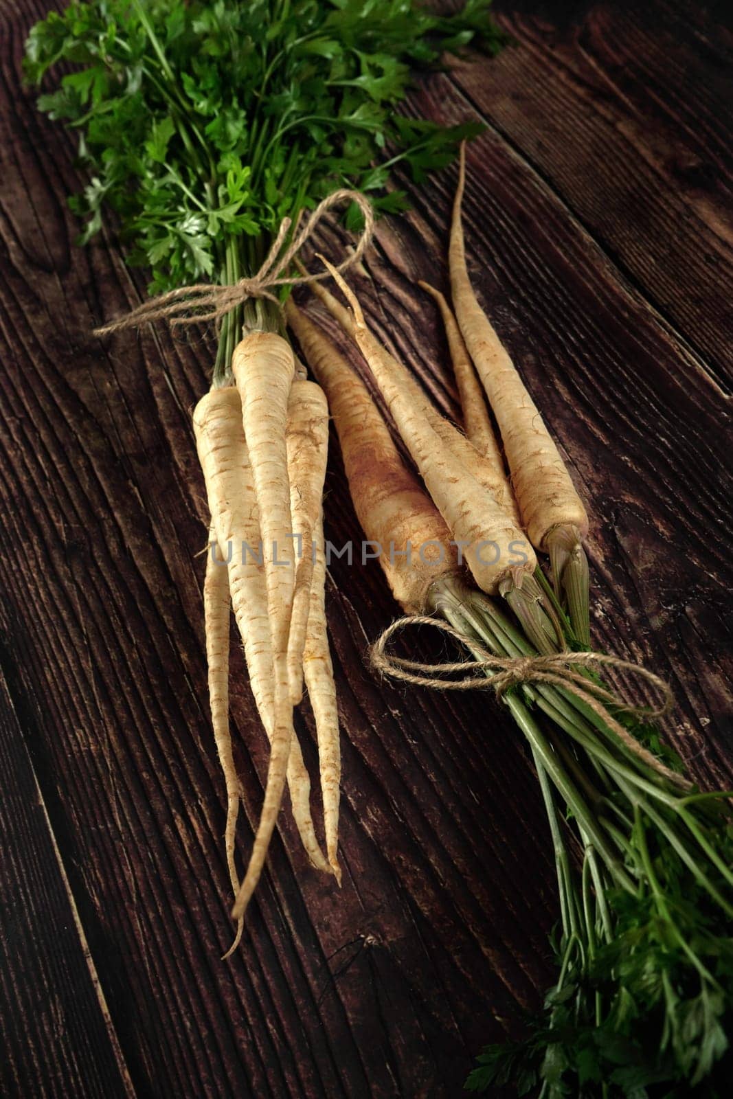 Parsley, parsnip roots with green leaves lying on dark wooden rustic table by Ivanko