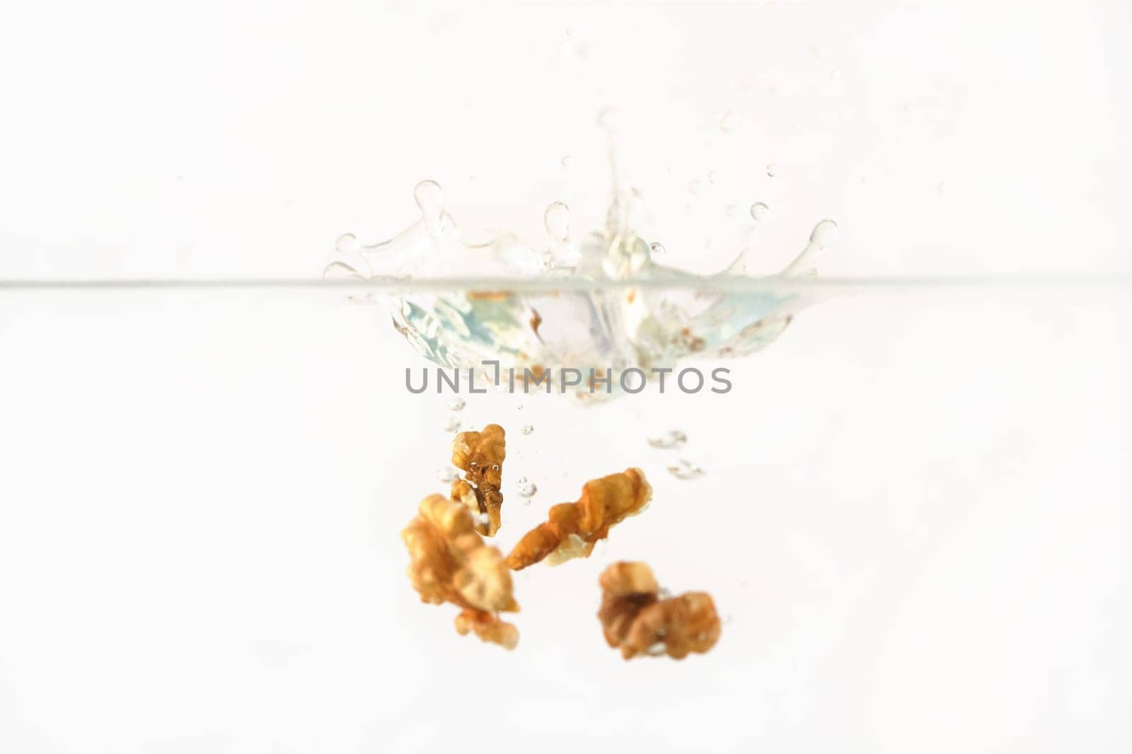 Walnut kernels dropped into water aquarium tank, high speed photo, white background by Ivanko