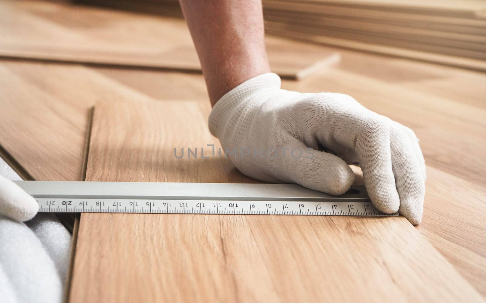 Installing laminated floor, detail on man hands in white gloves holding aluminium ruler over wooden tile