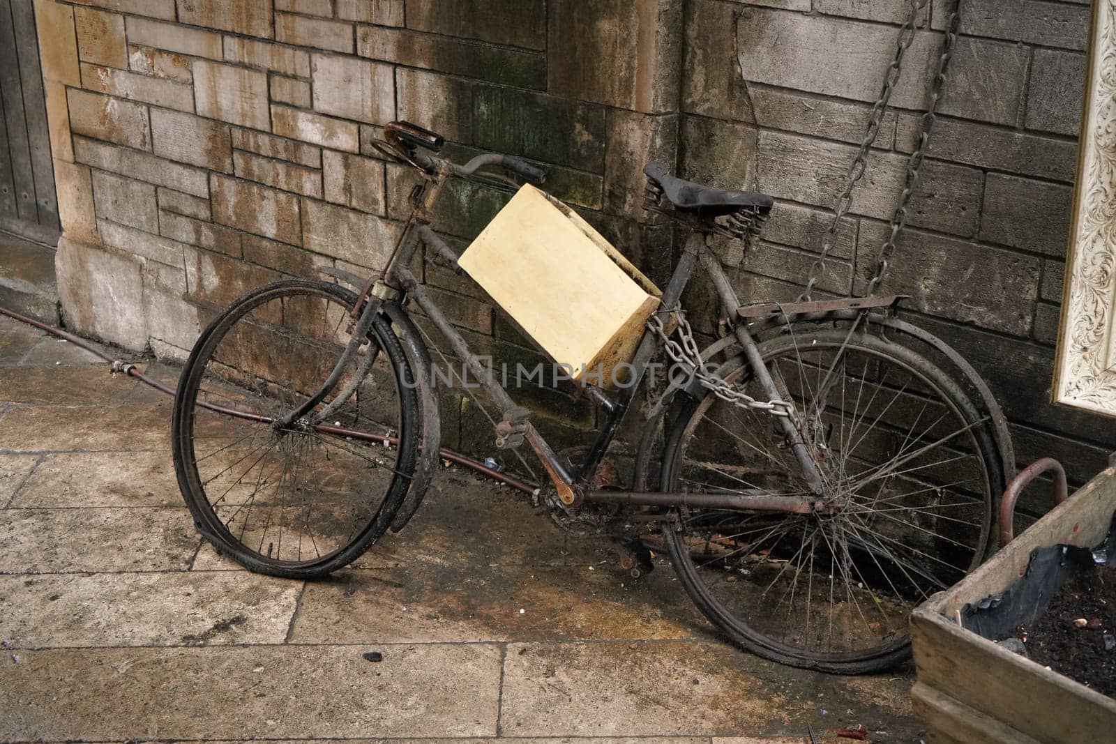 Unused rusty old black bicycle with wooden box parked near dirty brick wall