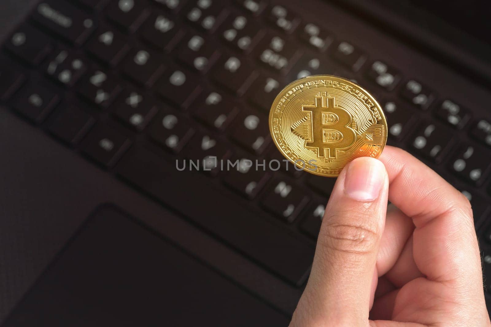 Woman hand holding golden coloured bitcoin coin over black laptop keyboard by Ivanko